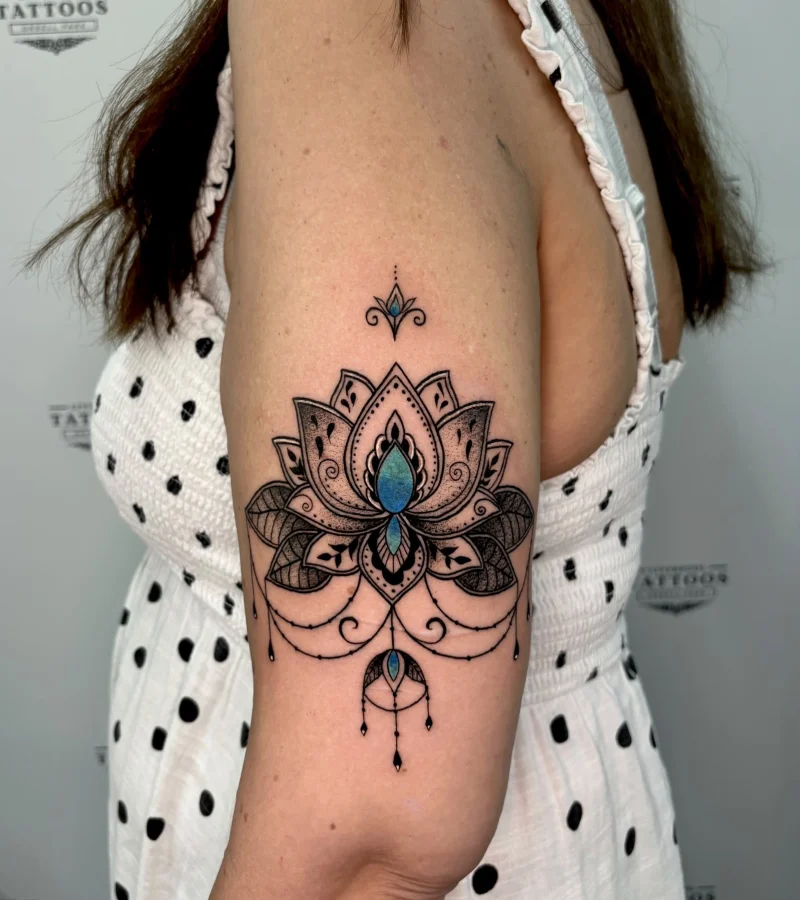 Ornamental mandala upper arm tattoo with blue color accents by Demi