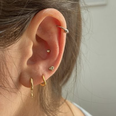 Minimalist conch piercing stud paired with gold lobe hoops and helix ring